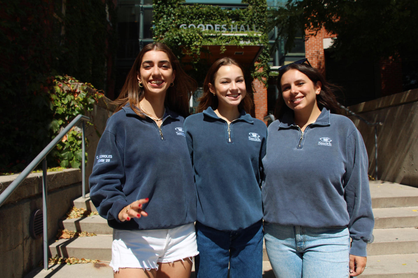 Three female OTD members in navy-blue Smith quarter-zips posing on the front steps of Goodes Hall